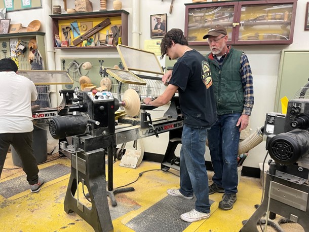 Senior Gabriel Hirsch working on his bowl project using the lathe with help from the teacher, Mr. Sorenson.