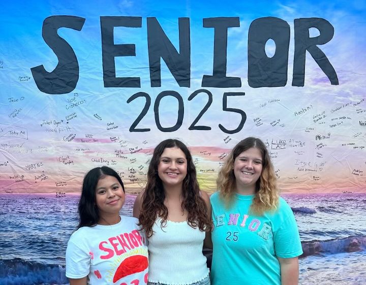 Seniors Sophie Canoe, Krystal Waters, and Lexi Quitain taking photos in front of posters made by leadership.