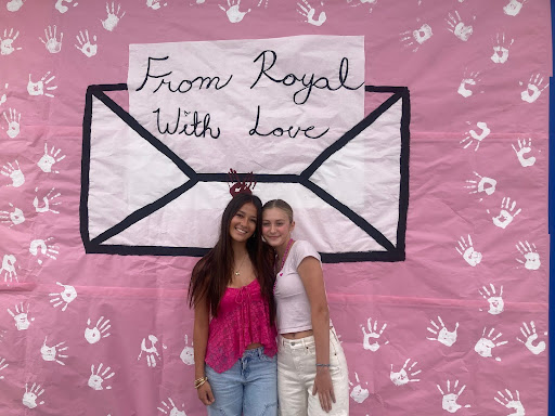 Juniors Grace Ae and Ella Copeland taking a picture in front of the pink out sign in front of the MPR, "To Royal With Love".